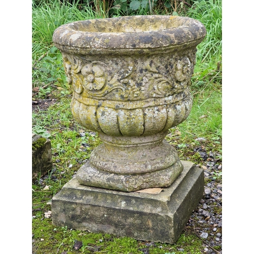 1013 - Pair of weathered reconstituted stone garden urns with floral relief and lobed bowls, raised on cham... 