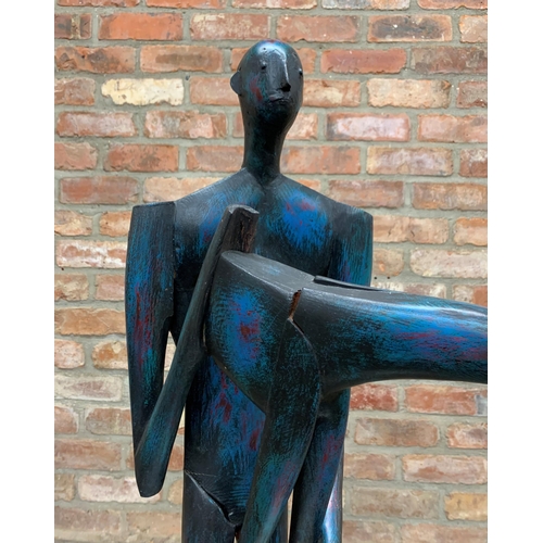 1380 - John Wragg (1937-2020) - Standing man holding a giraffe, painted wooded sculpture, 96cm high