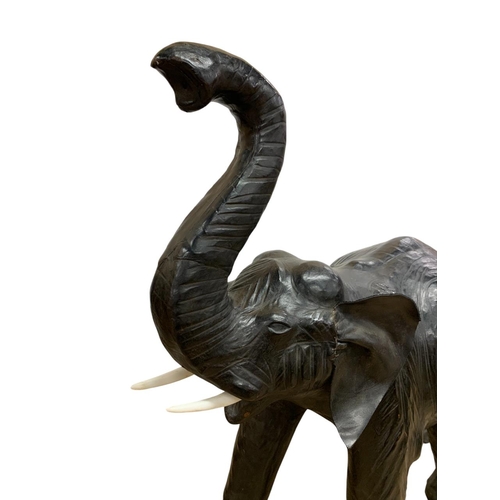 1465 - Pair of black leather elephant sculptures, in the manner of Liberty, each having original faux ivory... 