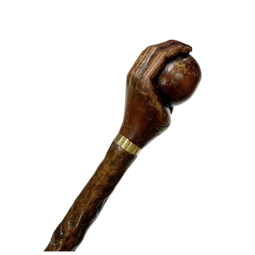 661 - Folk Art hazel wood walking cane with handle carved as a hand holding a ball, with thin metal collar... 