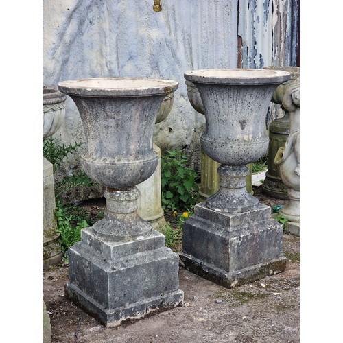 166 - Pair of weathered reconstituted stone garden urns with flared rims and chamfered square cut plinths,... 