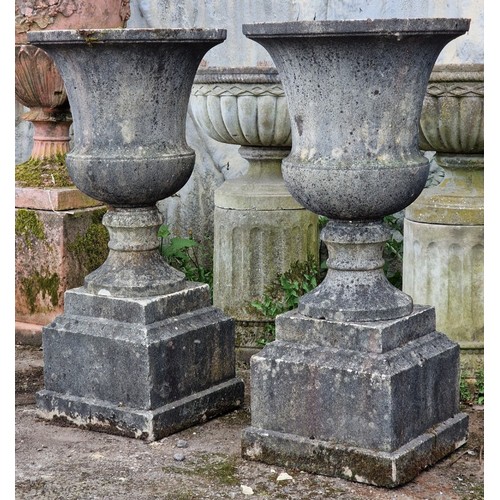 166 - Pair of weathered reconstituted stone garden urns with flared rims and chamfered square cut plinths,... 