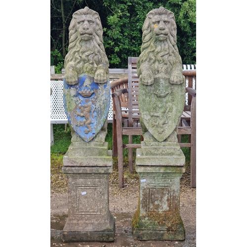 48 - Pair of weathered reconstituted stone garden statues of seated lions with shields, raised on square ... 