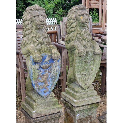 48 - Pair of weathered reconstituted stone garden statues of seated lions with shields, raised on square ... 