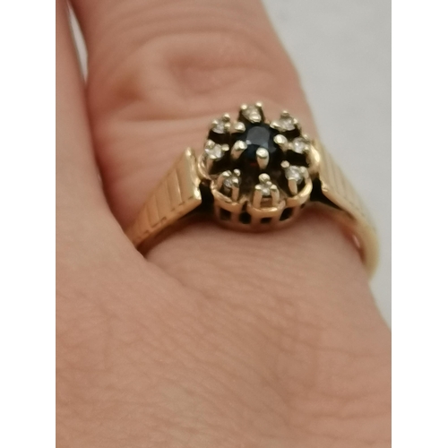 474B - A 9 carat gold cluster ring, the central blue stone surrounded by eight small white stones, in a fan... 