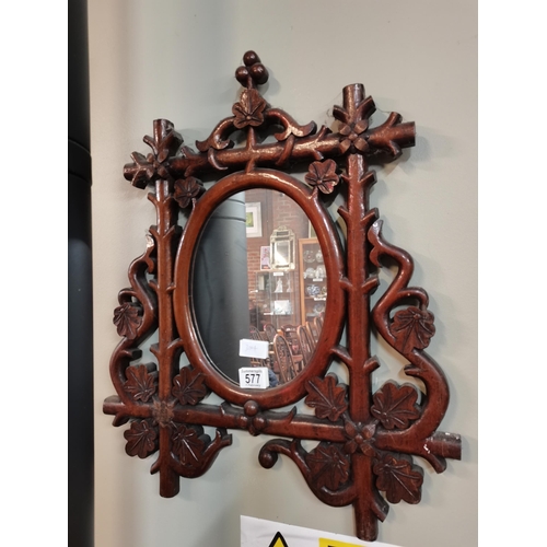 577 - A hardwood carved mirror, the oval mirror plate within an ornately carved frame of boughs and leaves... 