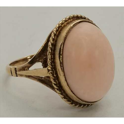 397B - A 9 carat gold pink hardstone ring, the large oval cabochon set with a rope-twist border to a raised... 