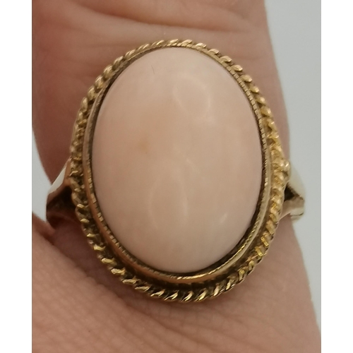 397B - A 9 carat gold pink hardstone ring, the large oval cabochon set with a rope-twist border to a raised... 