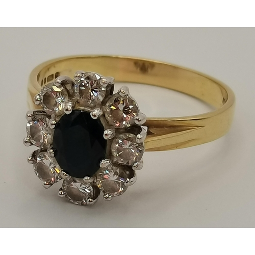 404 - An 18 carat gold diamond and sapphire cluster ring, the oval-cut sapphire enclosed by eight brillian... 