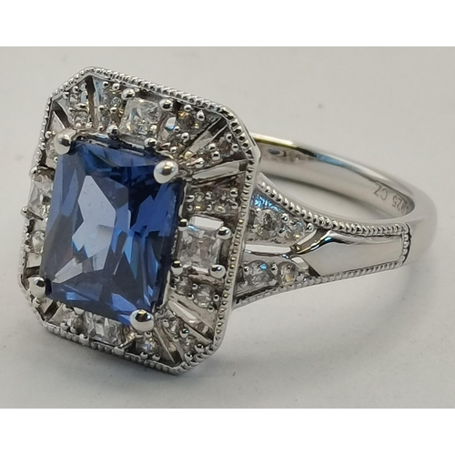 406B - A silver and cubic zirconia rectangular halo ring, the central rectangular blue stone enclosed by a ... 