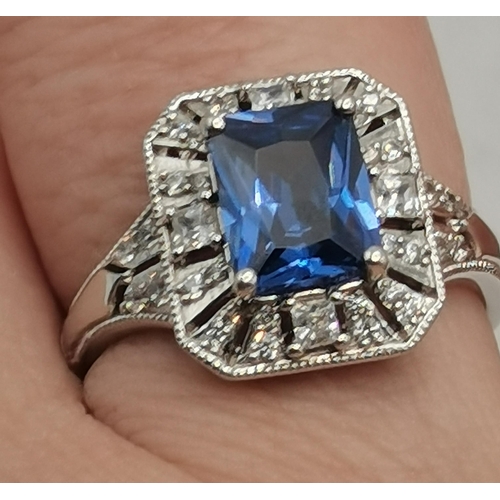 406B - A silver and cubic zirconia rectangular halo ring, the central rectangular blue stone enclosed by a ... 