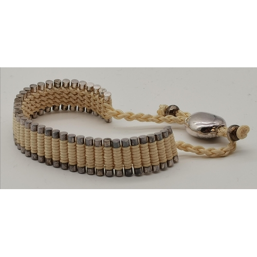 400 - A friendship bracelet by Links of London, the vertical cylinders bound by cream cord, with black clo... 