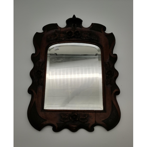 66 - An ornately carved mahogany wall mirror, 19th Century, the rectangular beveled glass with arched top... 