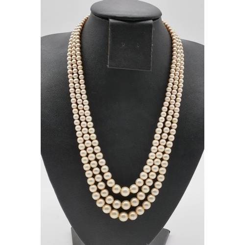 498 - A triple strand pearl necklace in hues of pink; together with two simulated pearl necklaces, one by ... 