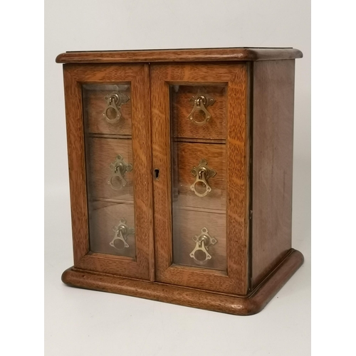 141 - A small oak tabletop cabinet, the pair of glazed doors opening to reveal three drawers with brass ha... 