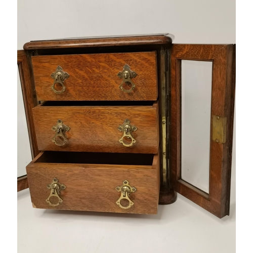 141 - A small oak tabletop cabinet, the pair of glazed doors opening to reveal three drawers with brass ha... 