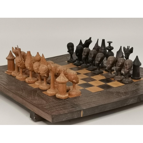 47 - An African wooden chess set, the broad board edge carved with figures and giraffes, the playing piec... 