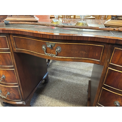 725 - A reproduction mahogany serpentine kneehole desk, the shaped top with gilt-tooled green leather writ... 