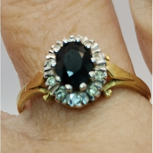 527A - An 18 carat gold blue and white stone cluster ring, the central oval stone enclosed by ten small rou... 