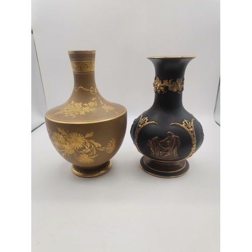 Two Wedgwood vases, the first a small bottle vase, the black ground with bronzed and gilded decoration in high relief; the second a shouldered small baluster vase with gilded floral decoration. (2) First 14.7cm