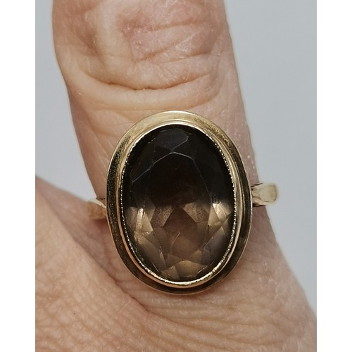  Two 9 carat gold rings, the first collet-set with an oval smoky quartz to pierced scroll shoulders, ... 