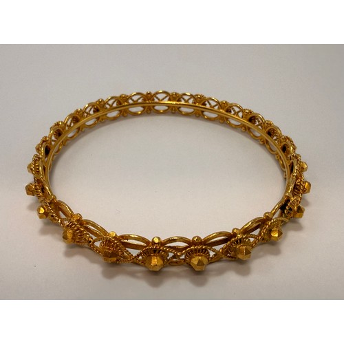  A fancy yellow metal openwork bangle, the inner bar set with circular links with blunted prunts at e... 