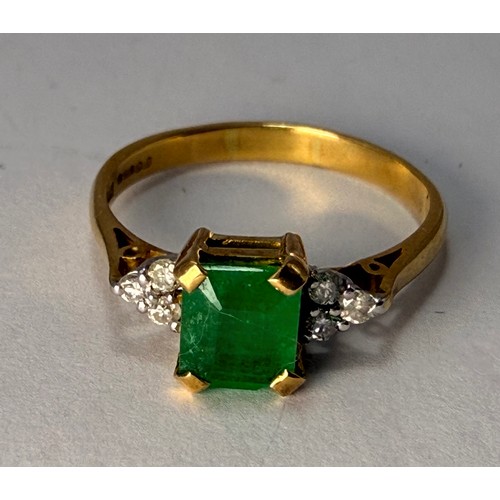  An 18 carat gold gemstone ring, claw-set with a central emerald-cut green stone flanked by a cluster... 
