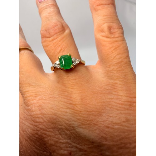  An 18 carat gold gemstone ring, claw-set with a central emerald-cut green stone flanked by a cluster... 