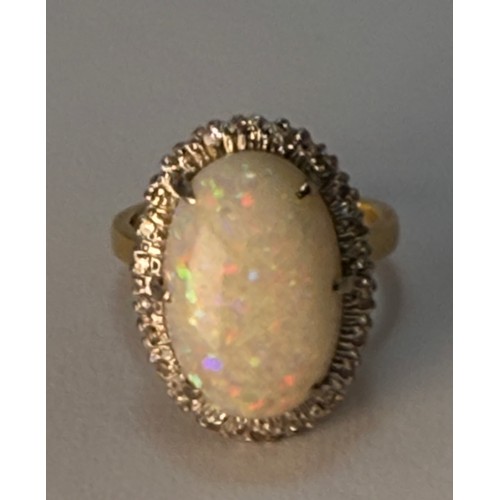 599 - A large opal and diamond cluster ring, the claw-set oval cabochon enclosed by a band of twenty-two e... 
