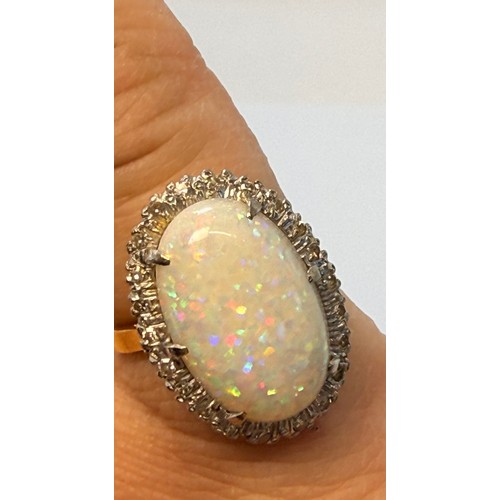 599 - A large opal and diamond cluster ring, the claw-set oval cabochon enclosed by a band of twenty-two e... 
