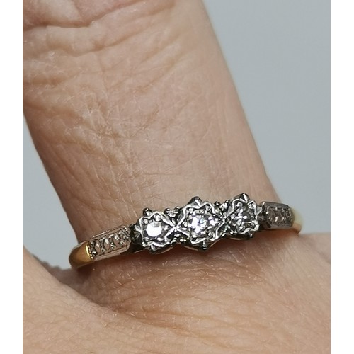  A three-stone ring, illusion-set with graduated round diamonds in a raised openwork mount with carve... 