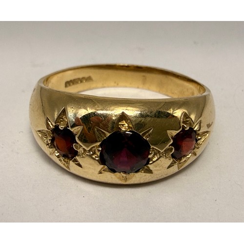  A 9 carat gold three-stone garnet ring, the broad tapering shank with a trio of graduated round ston... 