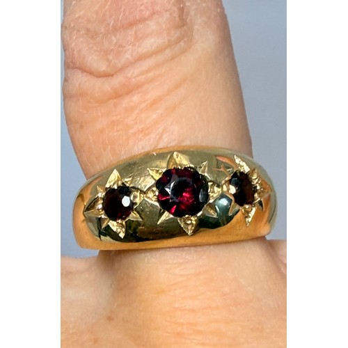  A 9 carat gold three-stone garnet ring, the broad tapering shank with a trio of graduated round ston... 