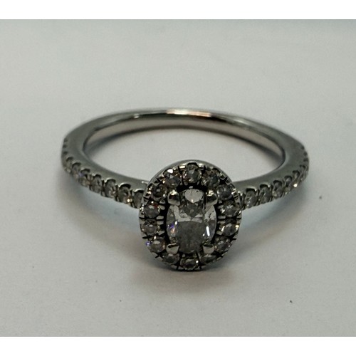  A platinum diamond engagement ring, the central oval brilliant cut stone enclosed by a halo of round... 