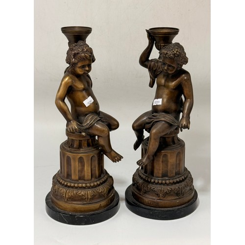 10 - A pair of bronze or spelter French candlesticks which are cherubs sitting on round bases