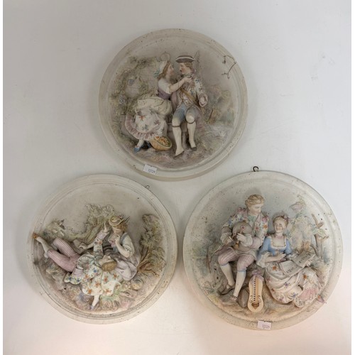 320 - Three bisque porcelain wall plaques featuring high-relief scenes of courting couples.  D 25 cm.