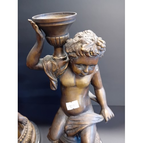 10 - A pair of bronze or spelter French candlesticks which are cherubs sitting on round bases
