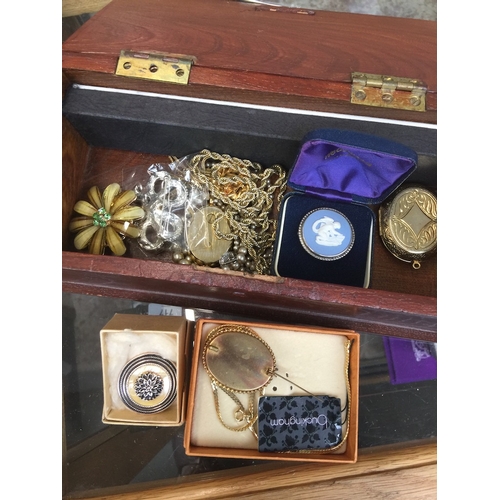 719 - A wooden box of costume jewellery including badges, brooches, a silver mounted Wedgwood cameo brooch... 