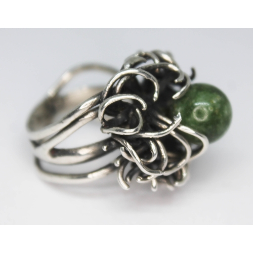 293 - A contemporary white metal ring with random wire setting supporting a jadeite bead, band unmarked, g... 