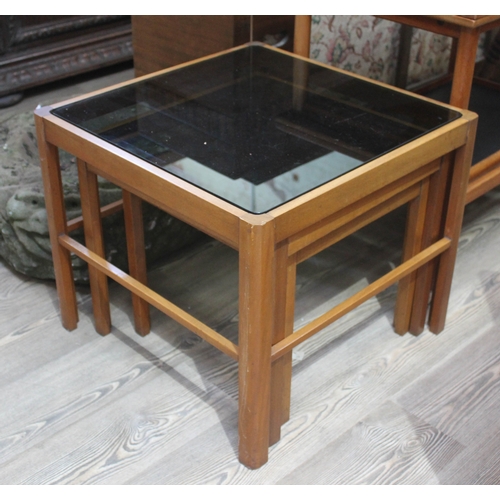 60 - A retro teak nest of tables with smoked glass tops.