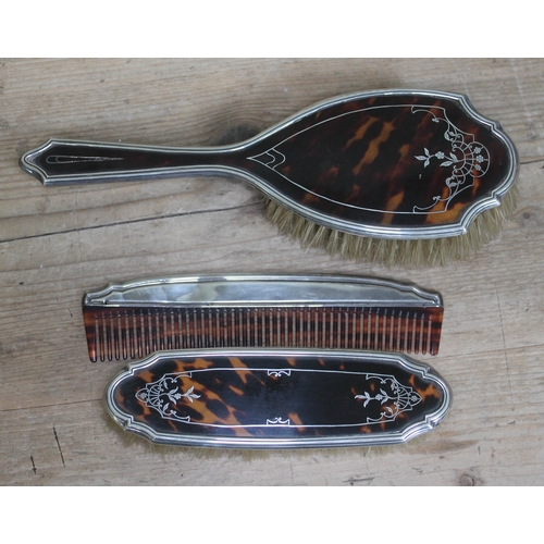 482 - A three piece hallmarked silver and tortoiseshell dressing table set comprising two brushes and a co... 