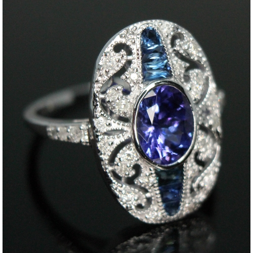 141 - A tanzanite, sapphire and diamond cluster ring, the central oval cut and bezel set tanzanite approx.... 