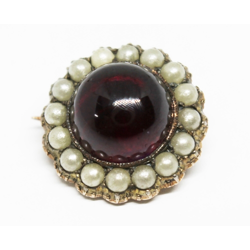 175 - A yellow metal brooch of flower head form set with a central purple garnet cabochon and surrounded b... 