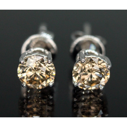 151 - A pair of diamond stud earrings, each four claw set round brilliant cut tinted diamond weighing appr... 