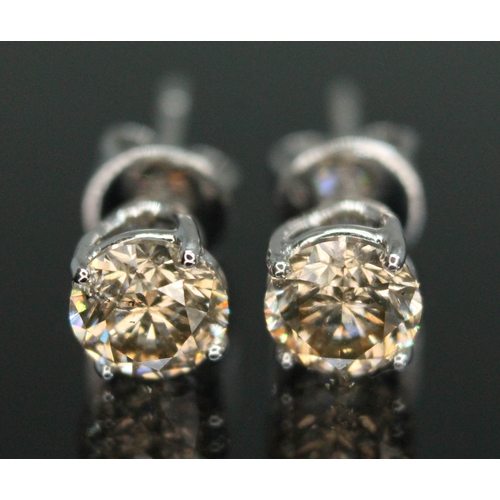 151 - A pair of diamond stud earrings, each four claw set round brilliant cut tinted diamond weighing appr... 