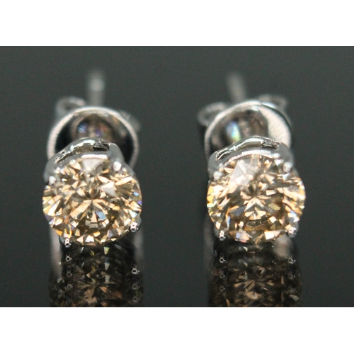 151 - A pair of diamond stud earrings, each four claw set round brilliant cut tinted diamond weighing appr... 