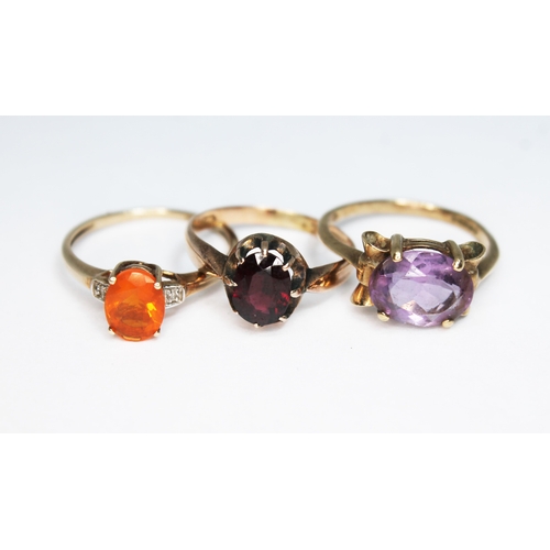 150 - A group of three rings comprising one set with an orange fire opal, one with a garnet and the other ... 