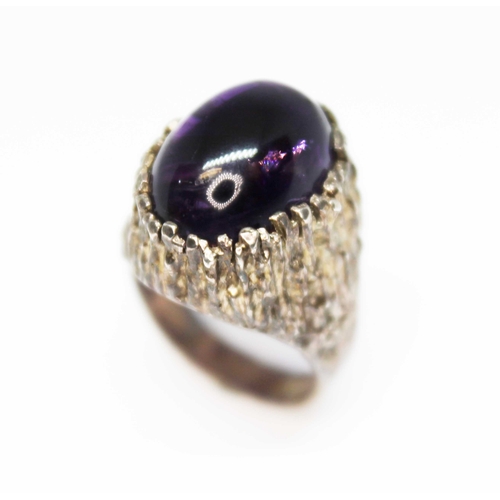 159 - A Modernist cast silver ring by Sidney Beddall, set with a large oval amethyst cabochon, sponsor's m... 