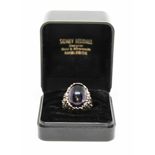 159 - A Modernist cast silver ring by Sidney Beddall, set with a large oval amethyst cabochon, sponsor's m... 