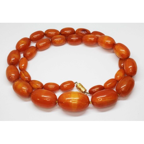 8 - A graduated butterscotch pressed amber bead necklace, the oval beads ranging in length from approx. ... 